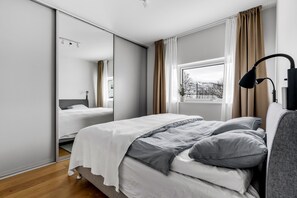 A bedroom with a bed, a bedside lamp, a window with curtains, and a mirror.