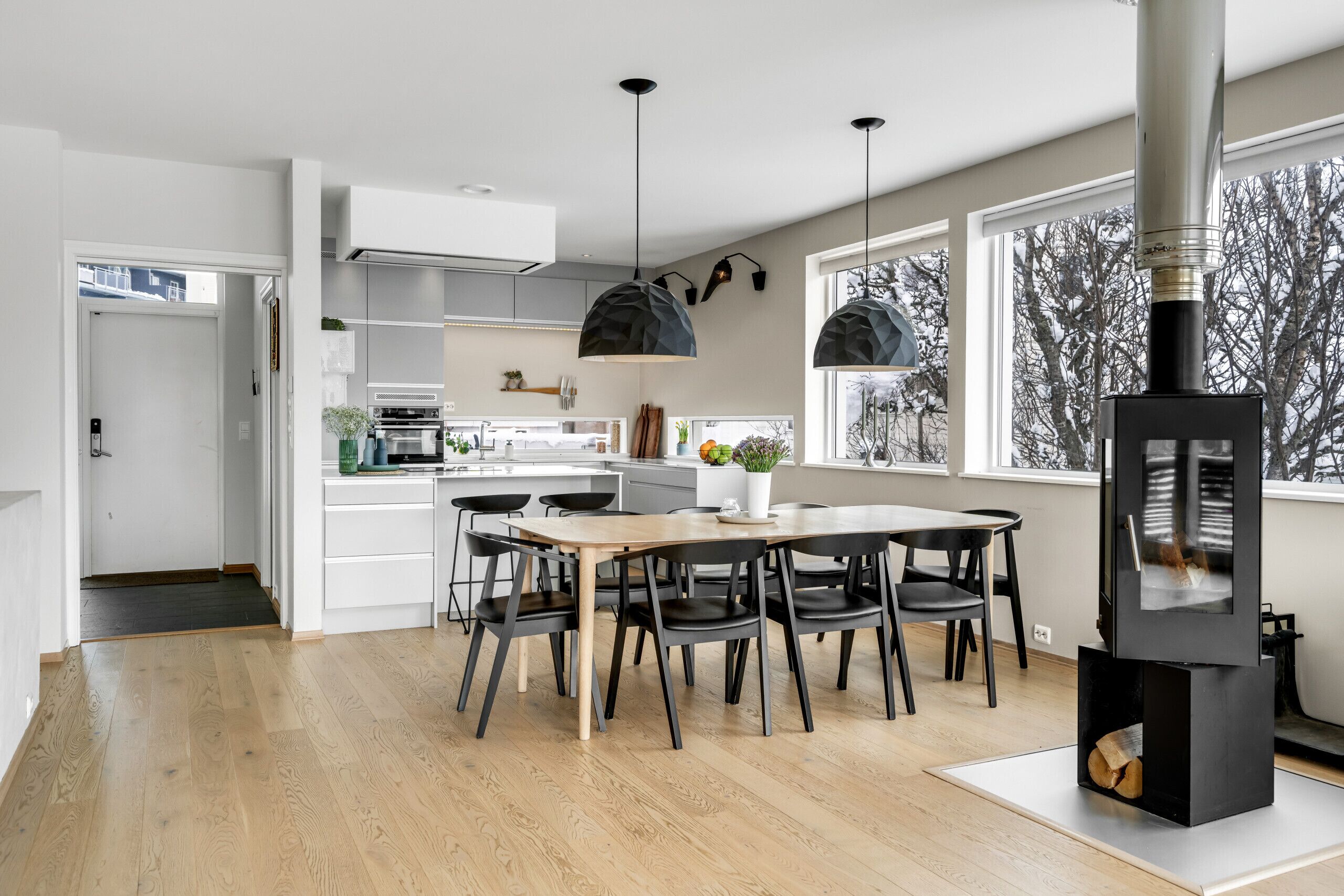 A modern kitchen with a dining table, chairs, pendant lights, and a wood-burning stove.