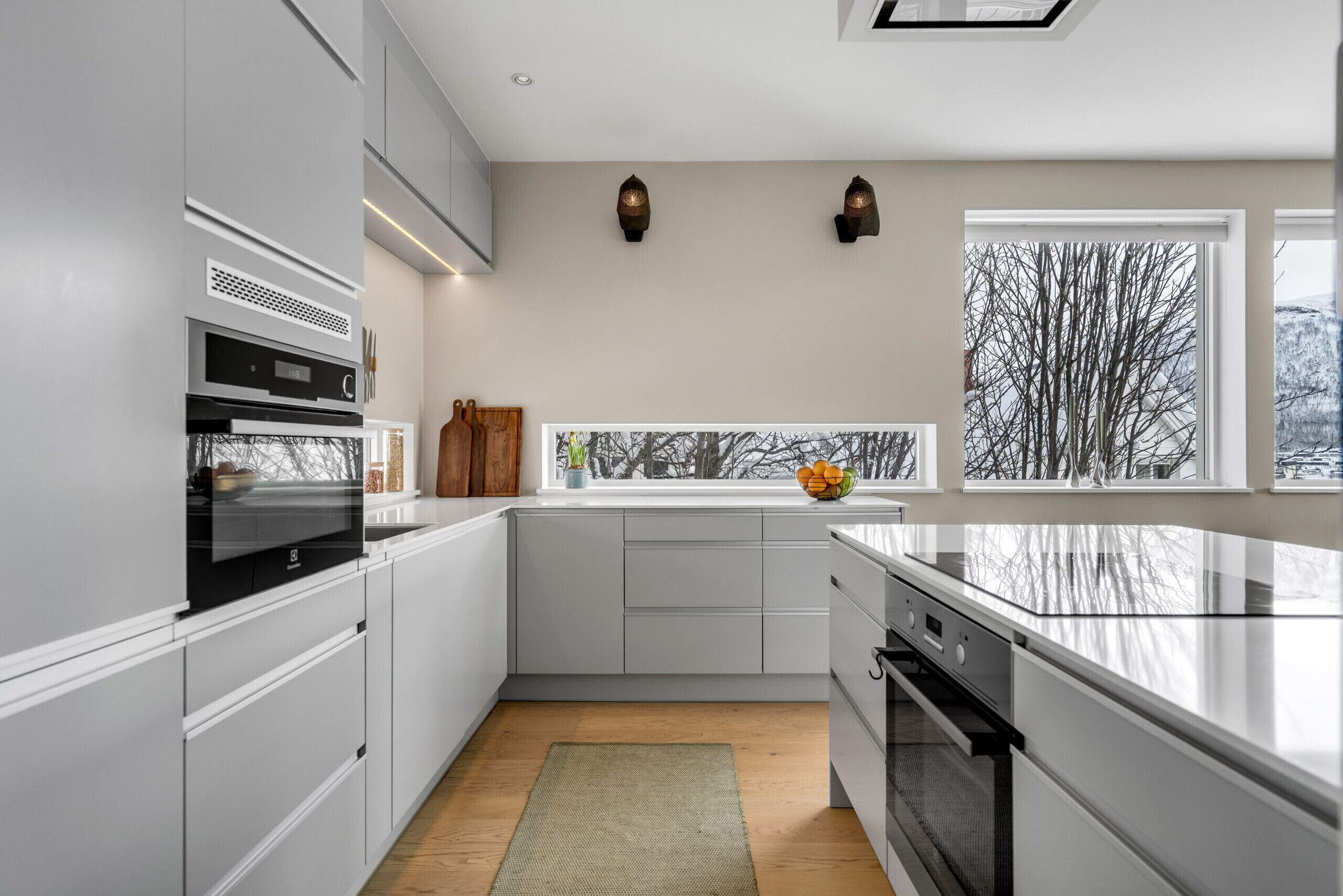 Een moderne keuken met inbouwapparatuur, een raam met uitzicht op bomen en een klein vensterbankje met decoratieve items.