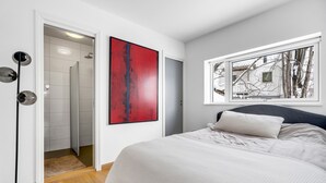 A bedroom with a bed, a window, a red abstract painting, and a door leading to a bathroom. - Northern Luxe Retreat (Tromsø)