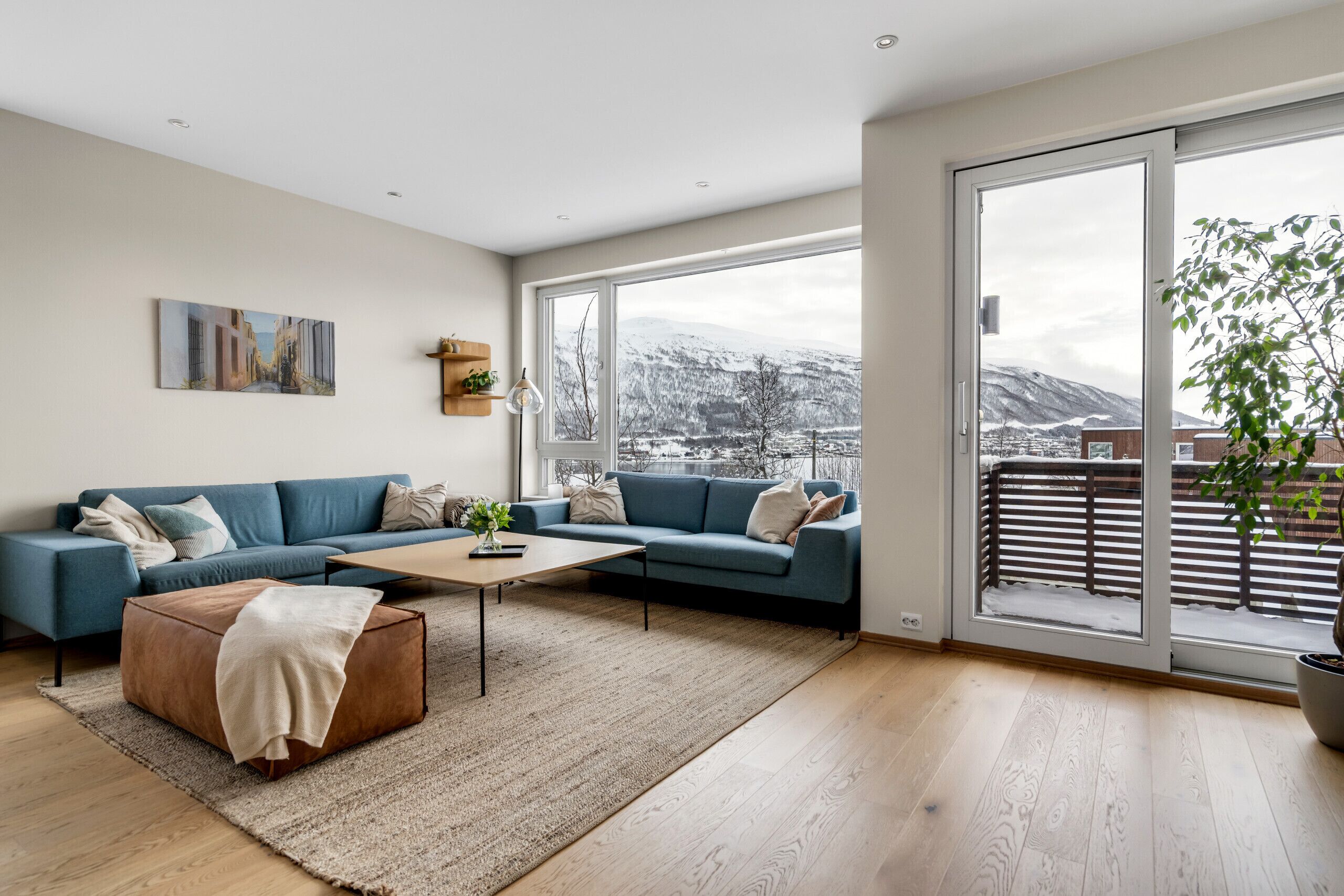 Un salon moderne avec un canapé, une table basse et une grande fenêtre donnant sur des montagnes enneigées.