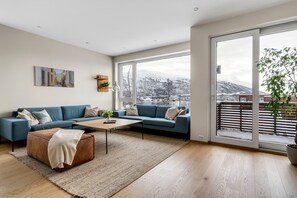 A modern living room with a sofa, coffee table, and a large window with a view of snow-covered mountains. - Northern Luxe Retreat (Tromsø)