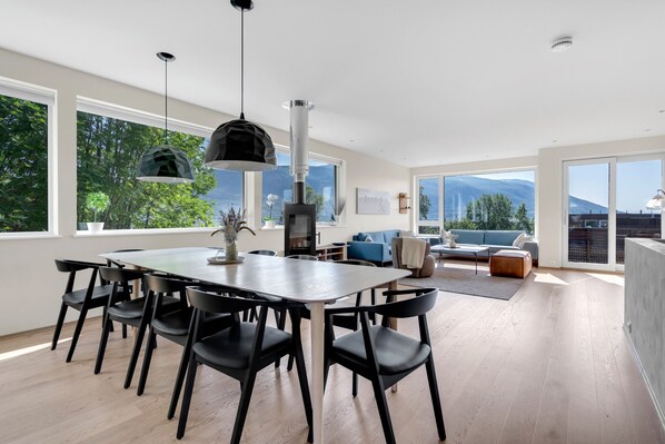 Un comedor moderno con una mesa grande y sillas, una lámpara colgante y vistas al exterior.