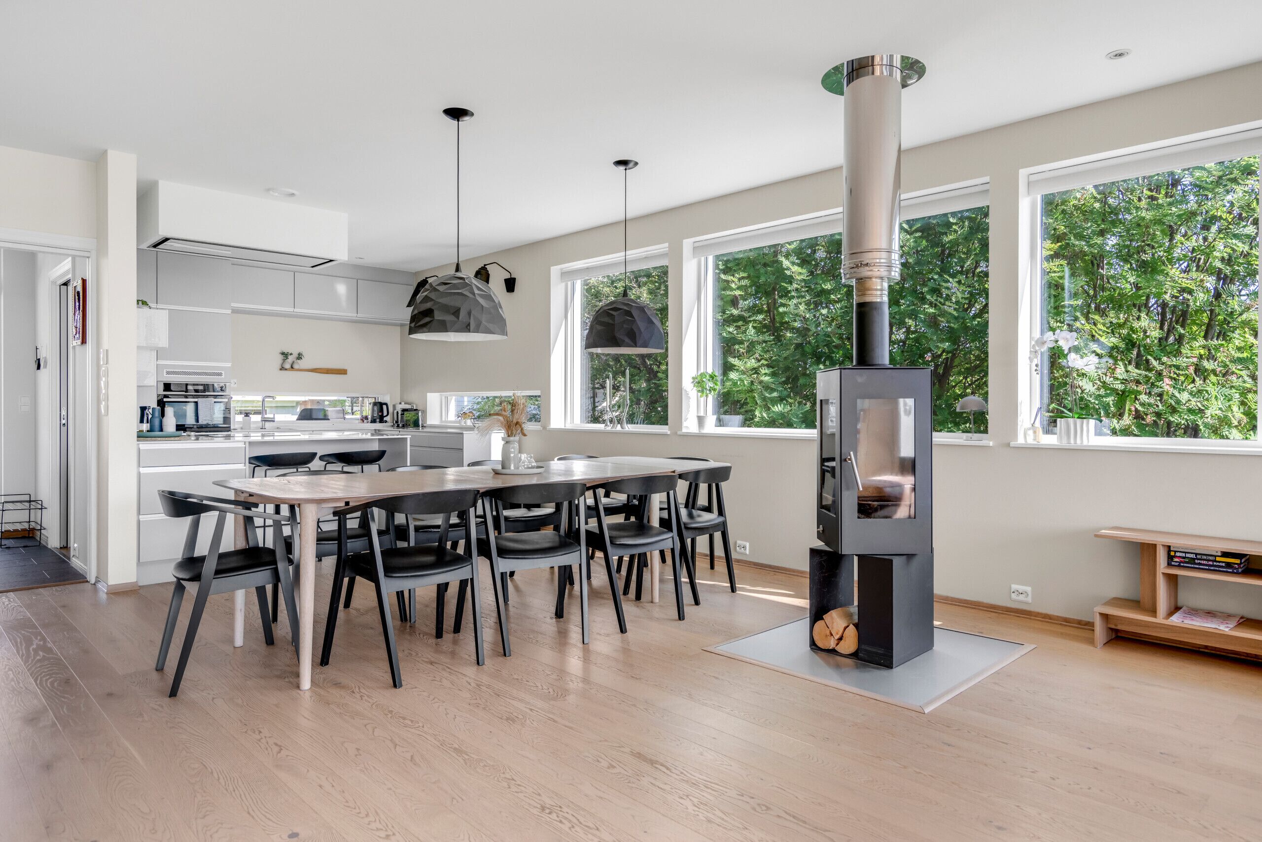 A modern kitchen with a central island, pendant lighting, and a large window overlooking greenery.