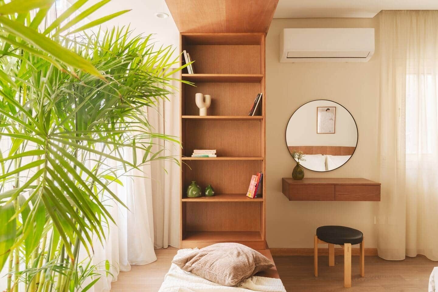 Un dormitorio con una estantería de madera, una mesita de noche, un espejo y una planta en maceta.