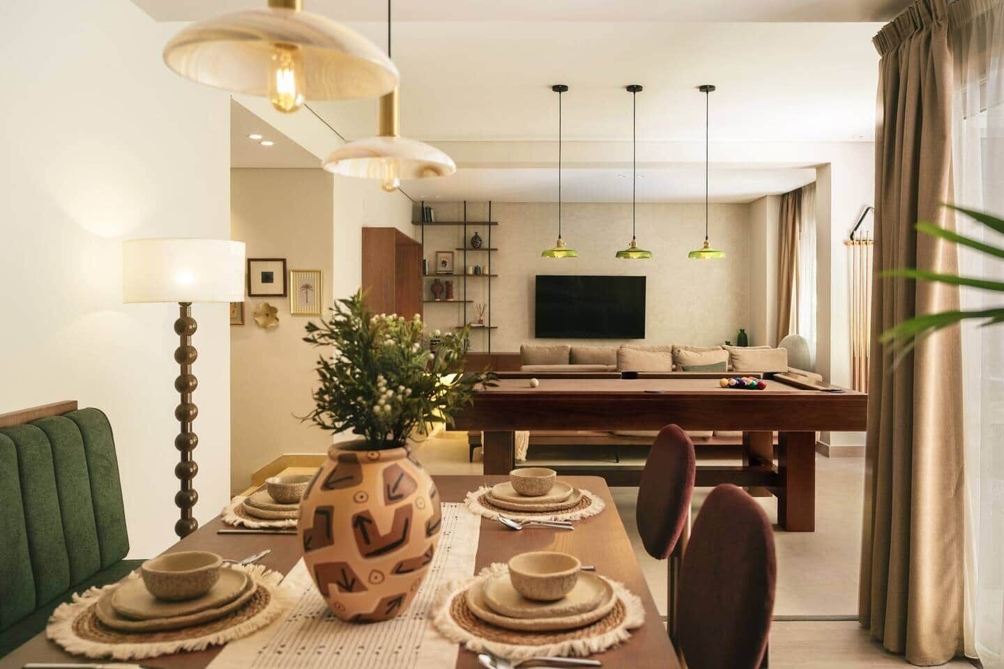 Uma área de refeições com mesa posta para quatro pessoas, um sofá, uma TV e mesa de bilhar.