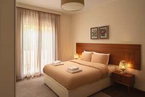 Ein Hotelzimmer mit einem großen Bett, zwei Nachttischlampen, einem Nachttisch und einem Fenster mit transparenten Vorhängen.