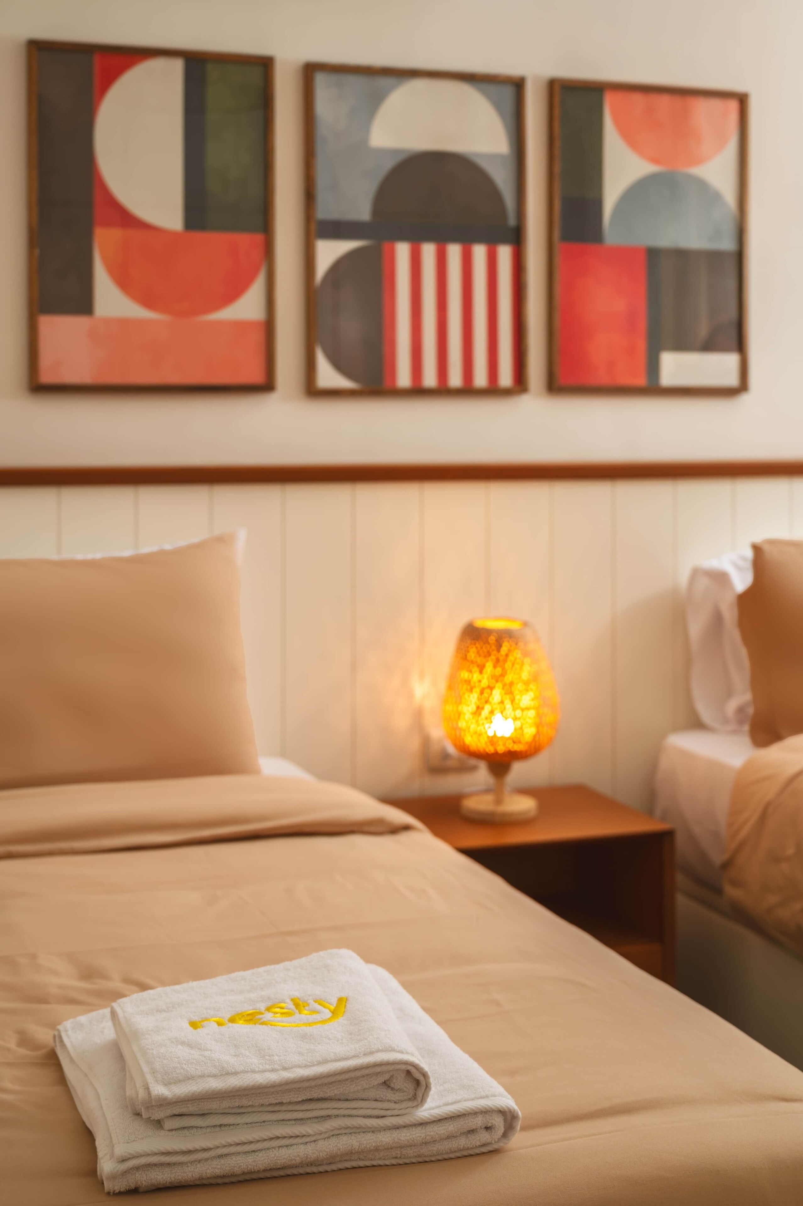 Une chambre d’hôtel avec un lit, une table de chevet avec une lampe et des œuvres d’art abstraites accrochées au mur.