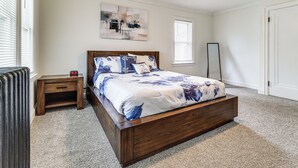 Un dormitorio con una cama de madera, una mesita de noche, un reloj de pared y un ventilador de techo.