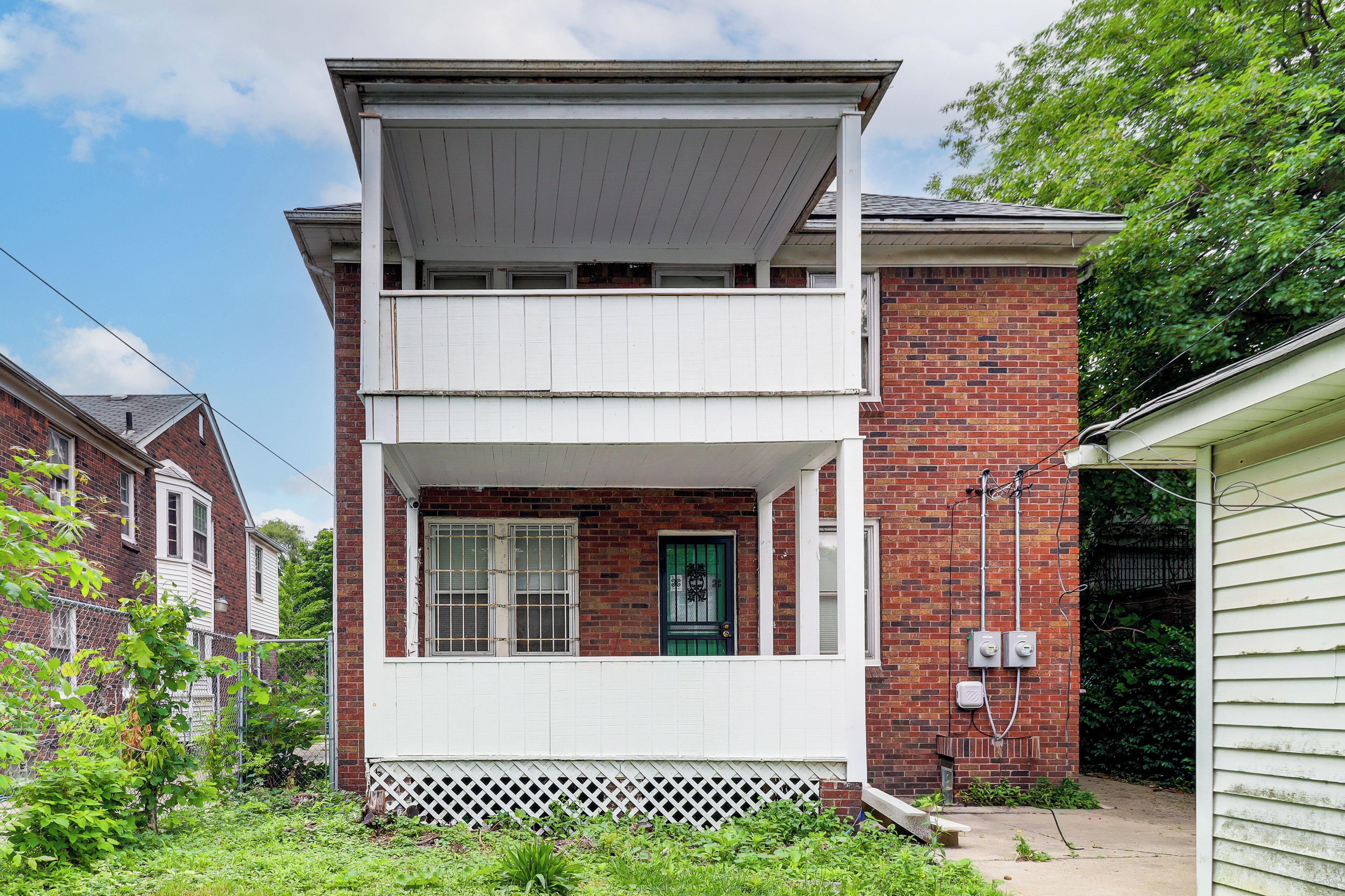 Une maison à deux étages avec un balcon, une porte verte et une véranda blanche.