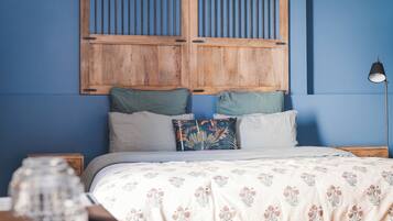 A bedroom with a wooden headboard, a bed with floral bedding, two pillows, a bedside lamp, and a nightstand with a glass jar.