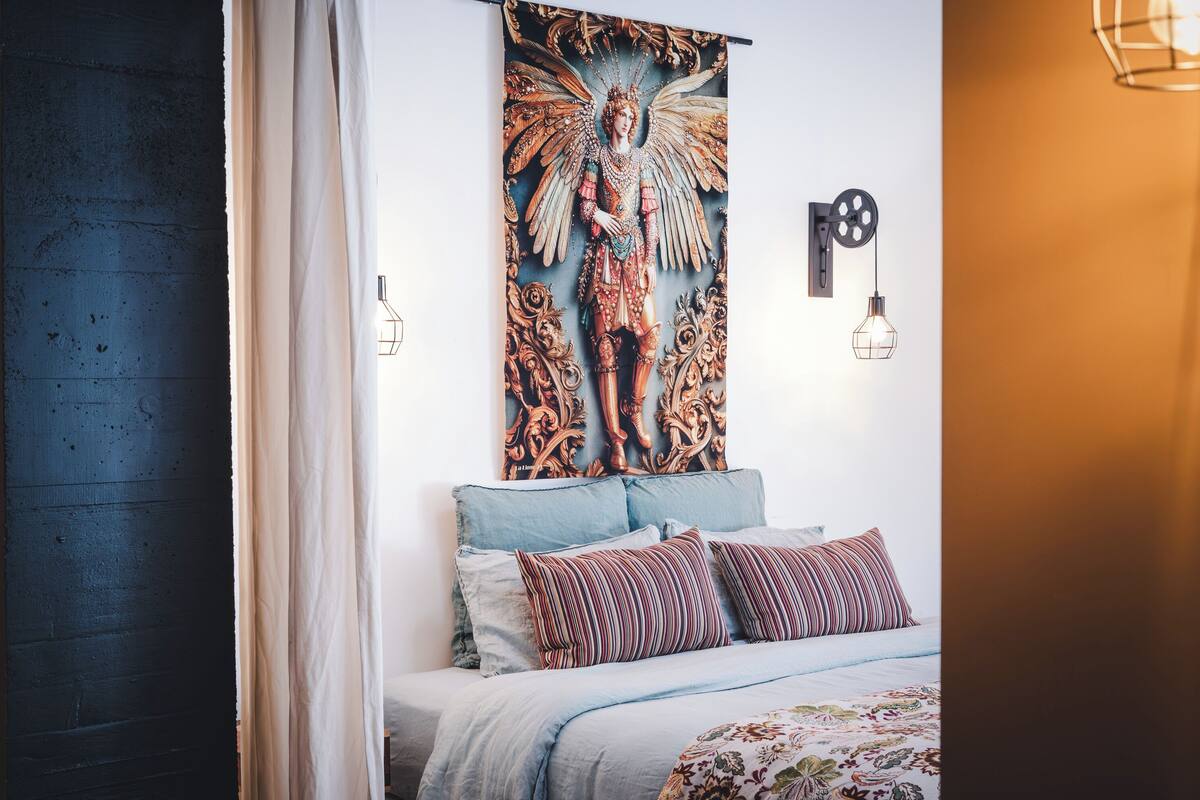 Un dormitorio con una cama, un tapiz y una lámpara fijada a la pared.