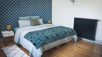 Une chambre à coucher avec un mur à motifs, un lit recouvert d’une couvre-lit à motifs, une table de chevet avec une lampe et un radiateur.