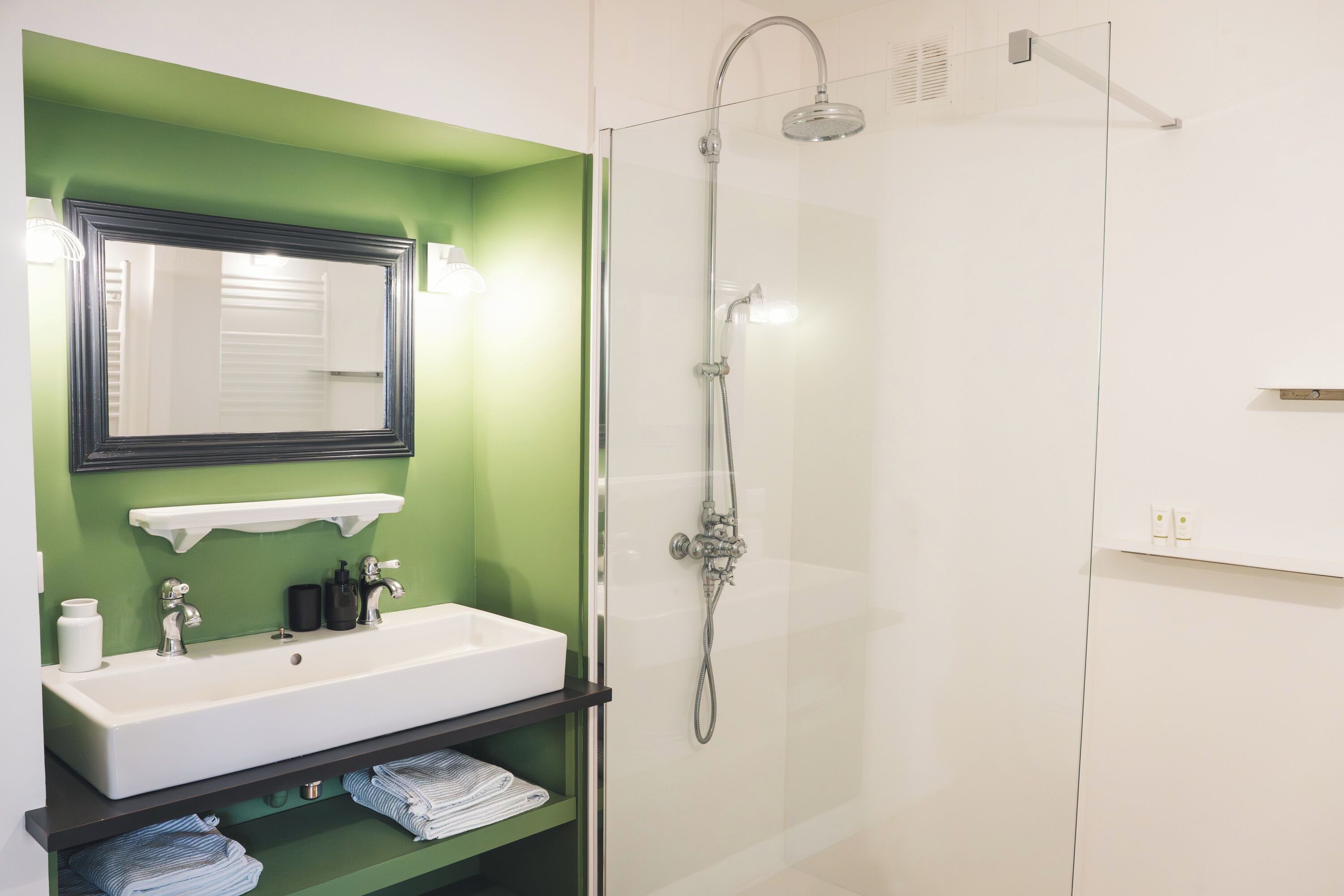 A bathroom with a white sink, green walls, a glass shower enclosure, and a mirror above the sink.