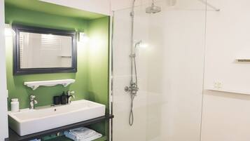 A bathroom with a white sink, green walls, a glass shower enclosure, and a mirror above the sink.