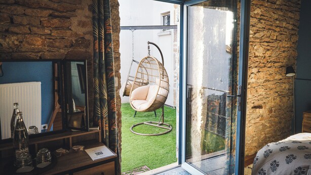 Um quarto com parede de pedra, cômoda de madeira, cadeira suspensa e porta de vidro que dá para o exterior.