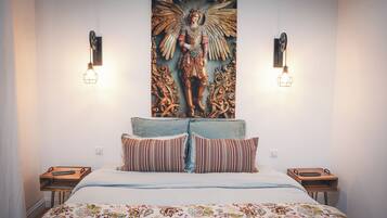Een slaapkamer met een bed, gestreepte kussens, een decoratief wandtapijt en twee wandlampen.