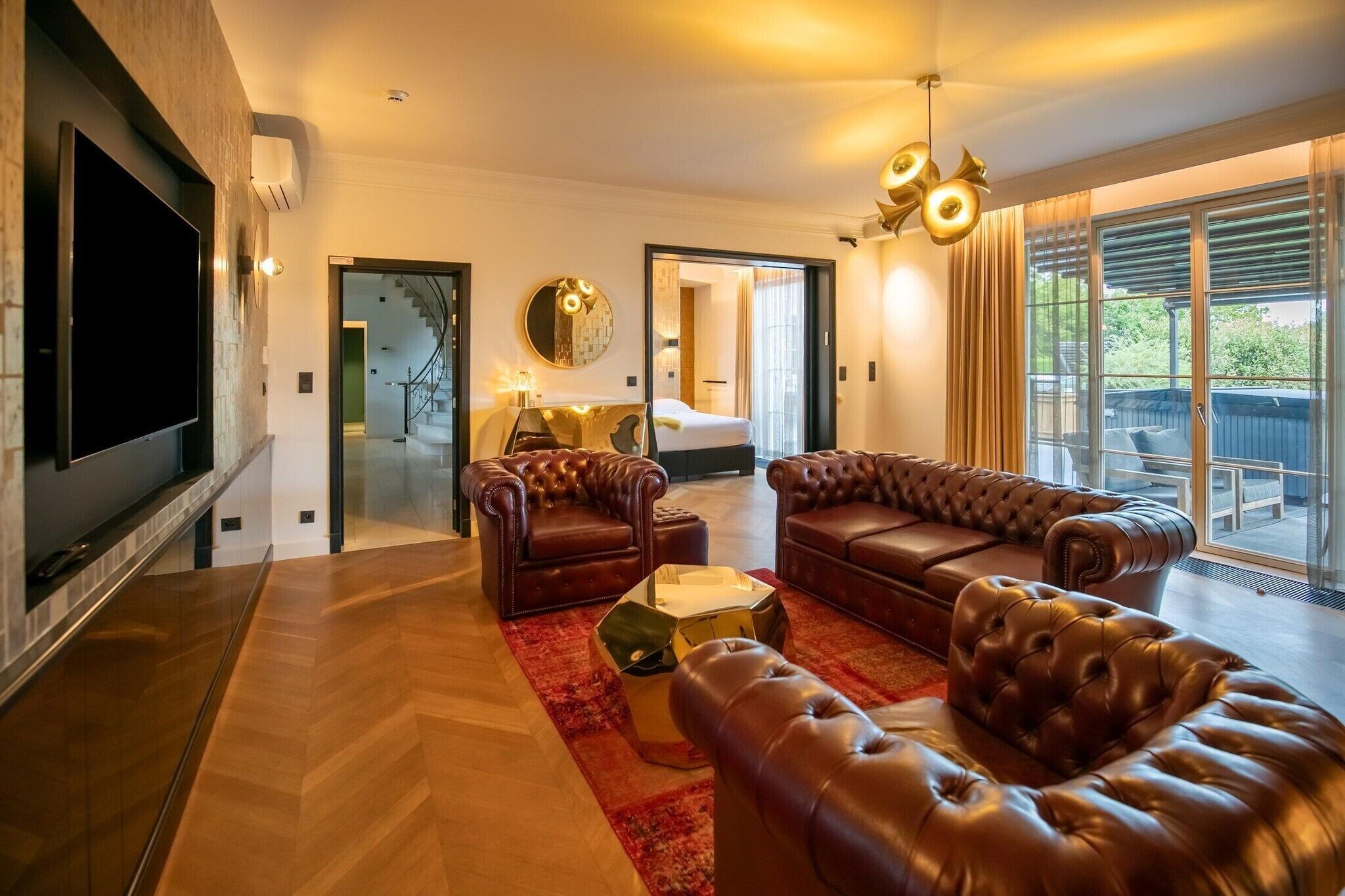A modern living room with leather sofas, a flat-screen TV, and a large window with a view.