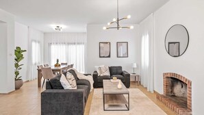 Een moderne woonkamer met een open haard, een eethoek met een tafel en stoelen, en een bank met decoratieve kussens.