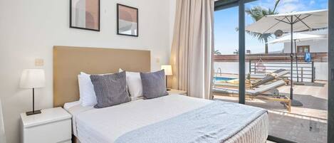 A hotel room with a bed, a nightstand, a lamp, and a view of a pool area.