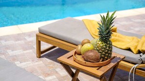 Een terras bij het zwembad met een houten tafel waarop een ananas, kiwi en kokosnoot liggen.