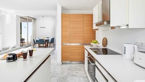 A modern kitchen with white cabinetry, a wooden accent wall, a dining area with blue chairs, and a coffee maker on the counter. - Akamé Luxury Beach Villa by Nomads (Paphos)