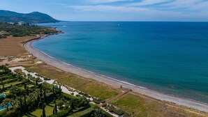 An aerial view of a coastal area with a beach, a landscaped garden, and a mountain in the background. - Akamé Luxury Beach Villa by Nomads (Paphos)
