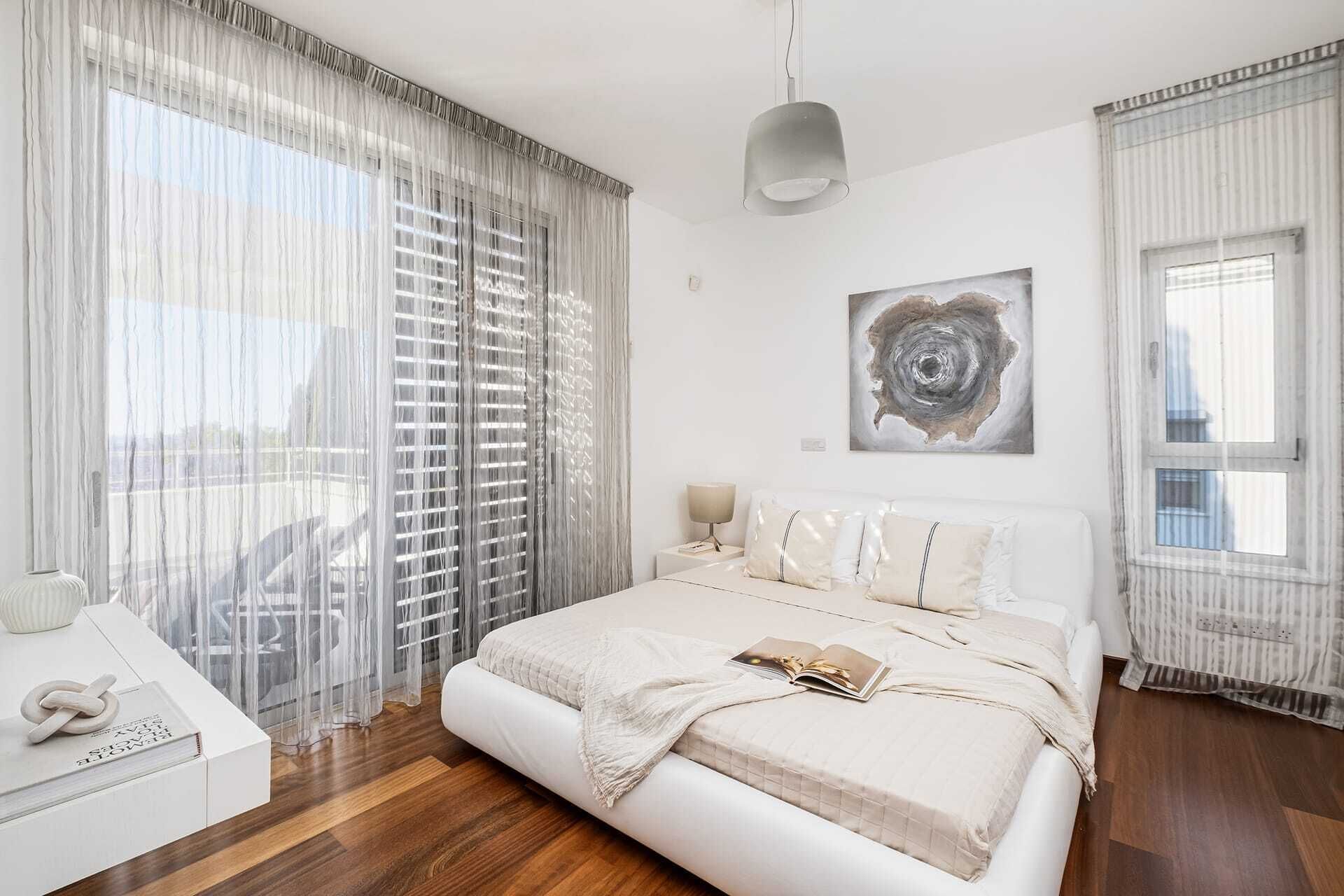 A bedroom with a bed, a bedside table, a lamp, and a window with curtains.