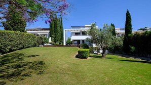 A modern two-story house with a well-maintained lawn, a hedge, and a tree with purple flowers. - Akamé Luxury Beach Villa by Nomads (Paphos)