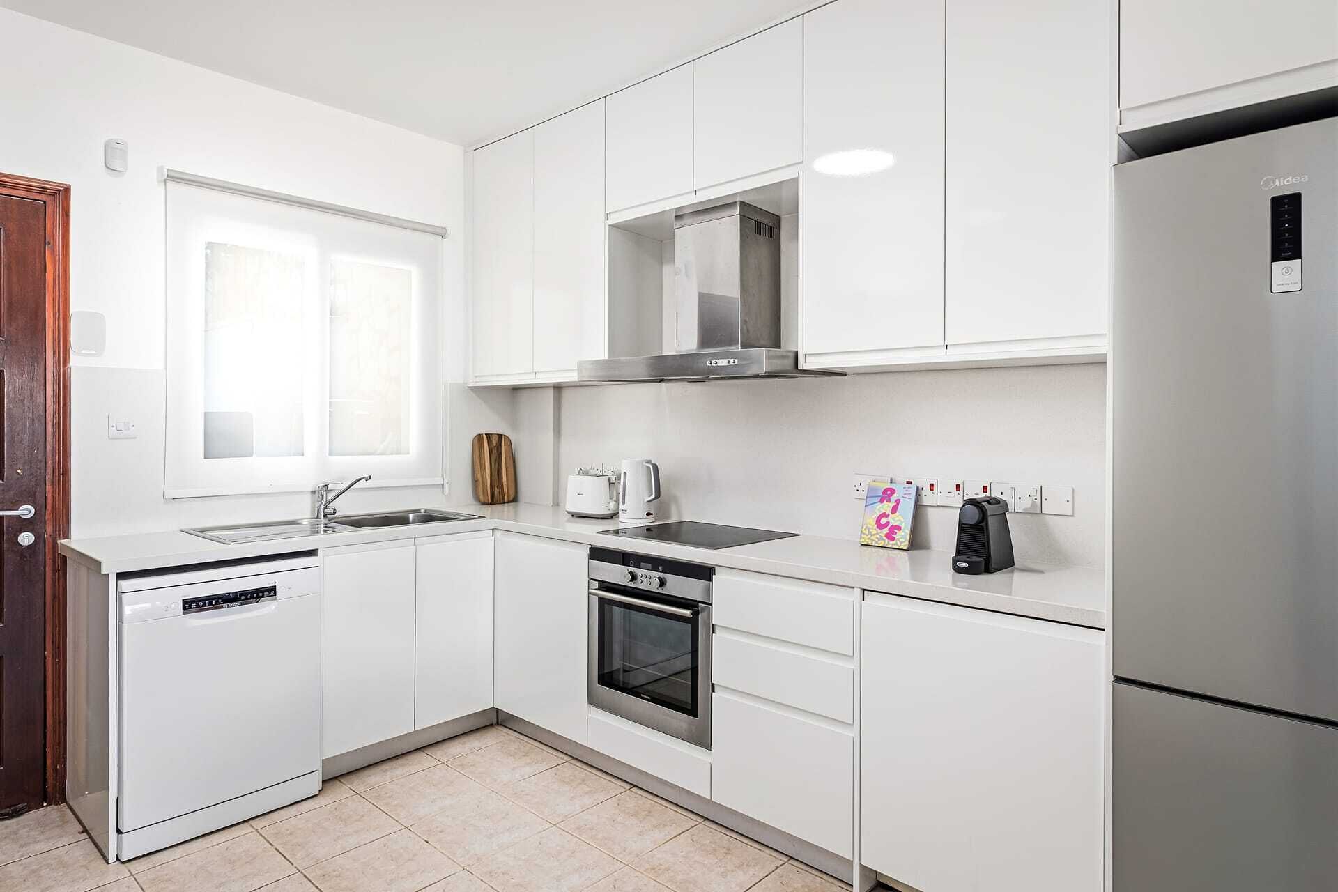 Cozinha moderna com armários brancos, lava-louças, forno, micro-ondas embutido e frigorífico.