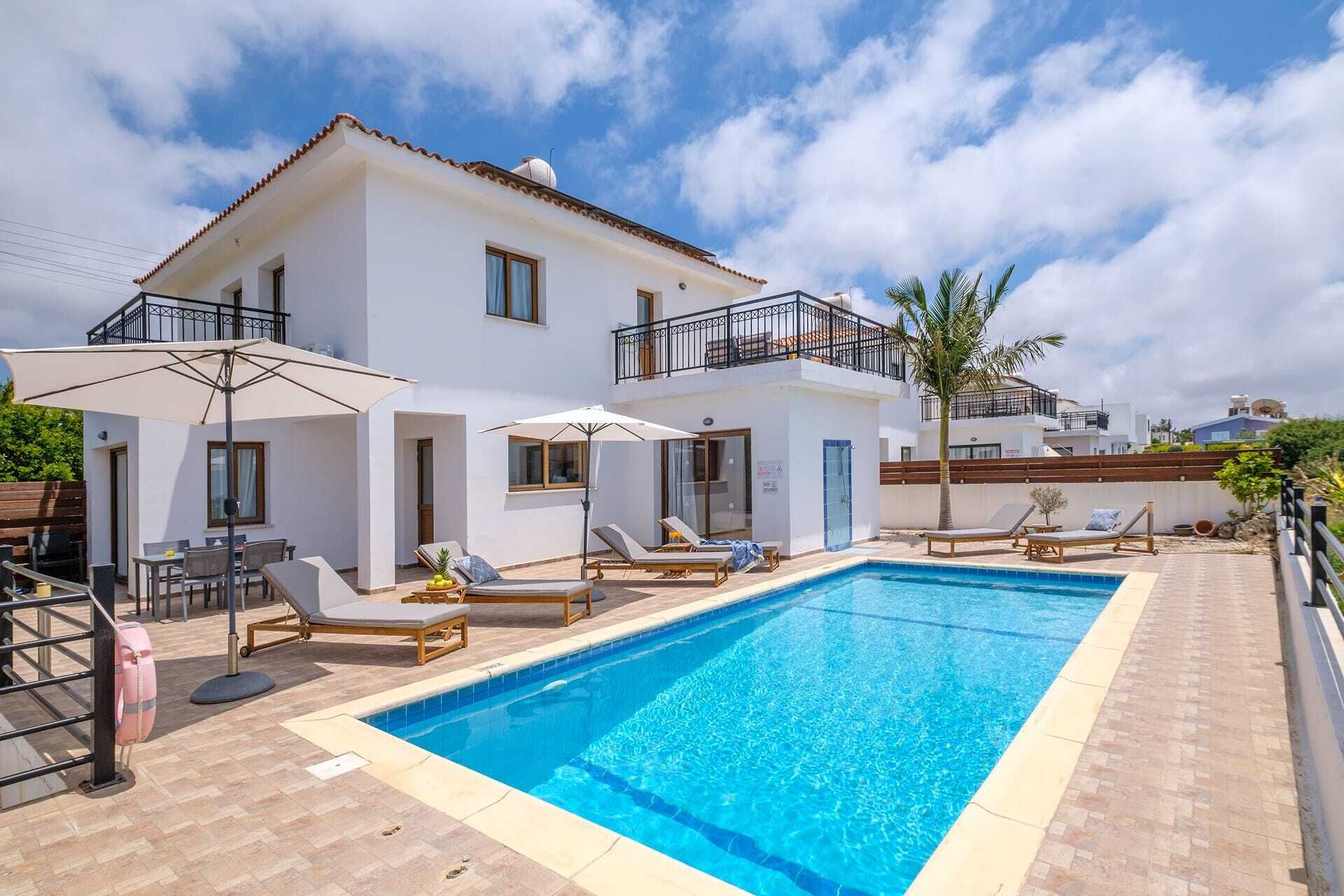 Un edificio blanco de dos plantas con piscina, zona de estar exterior y balcón.