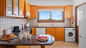 Una cocina con armarios de madera, un ventanal, una lavadora y una encimera con alimentos.