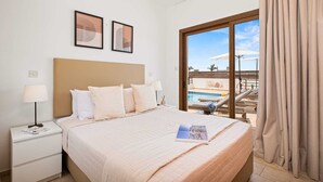 Habitación de hotel con cama, mesita de noche, lámpara y vista a una piscina y zona exterior.