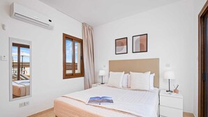 Una habitación de hotel con cama, mesita de noche, ventana con cortinas, aire acondicionado de pared y obras de arte enmarcadas.
