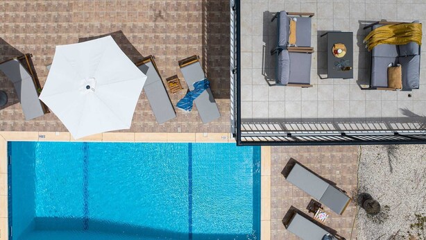 Vista aérea de un área de piscina en la azotea con sillones, sombrillas y una piscina.