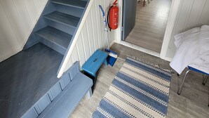Un escalier menant à une salle à manger, où l’on trouve un extincteur, une marche bleue et un tapis à motifs.