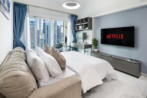 Ein modernes Schlafzimmer mit einem großen Bett, einem Schreibtisch, einem Fernseher und Blick auf die Stadt.