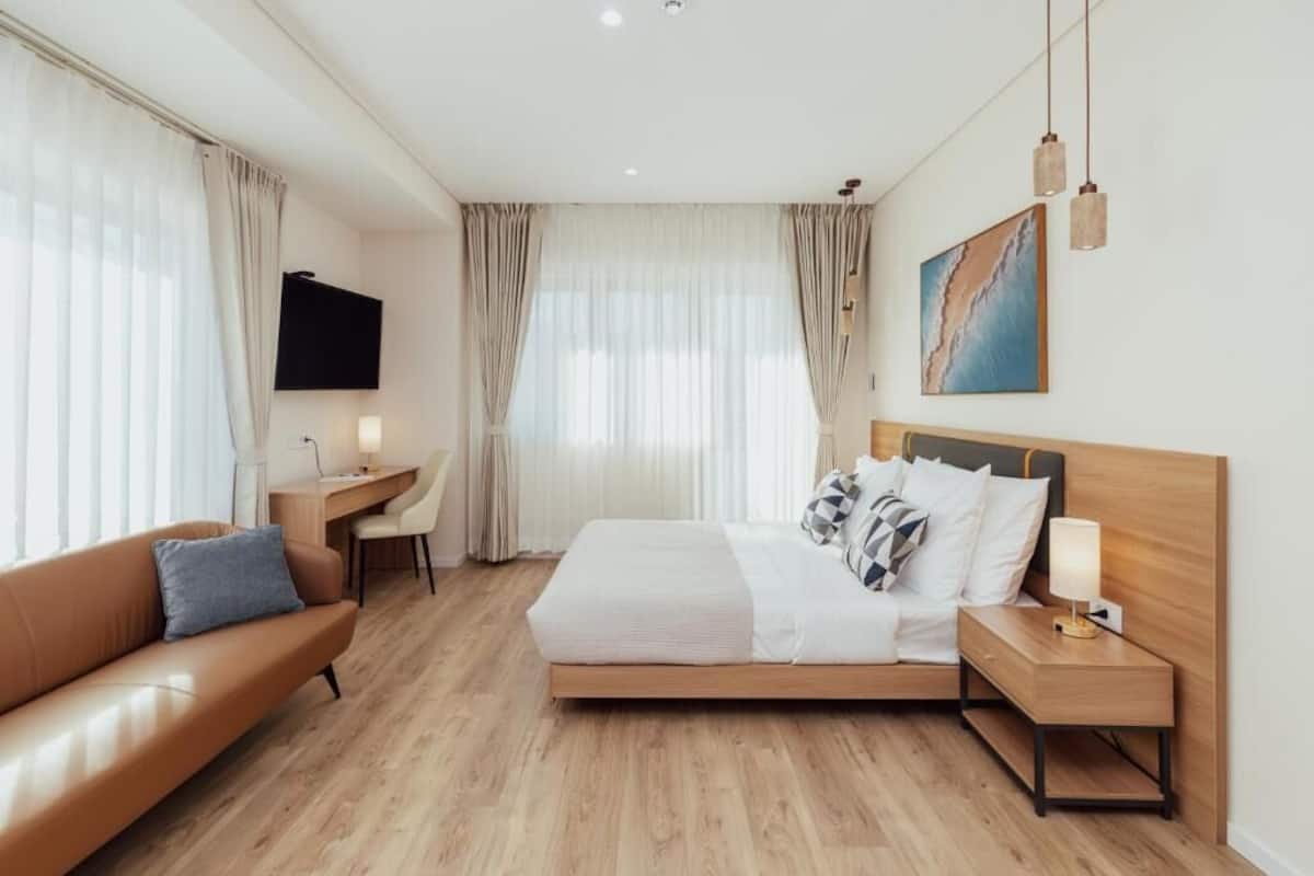 A hotel room with a bed, a desk, a chair, a sofa, and a TV.