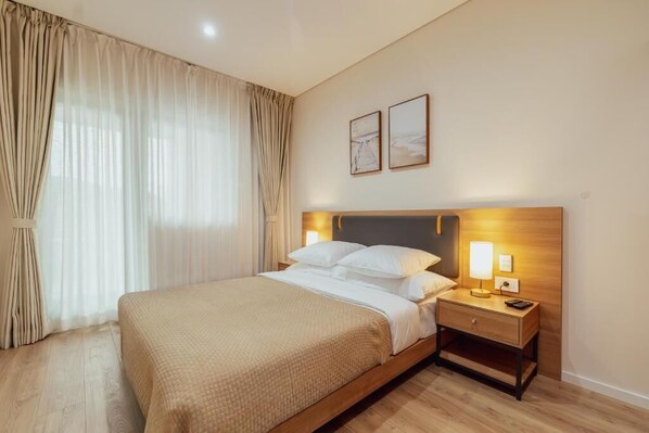 Une chambre d’hôtel avec un lit, une table de chevet, une lampe et des rideaux.