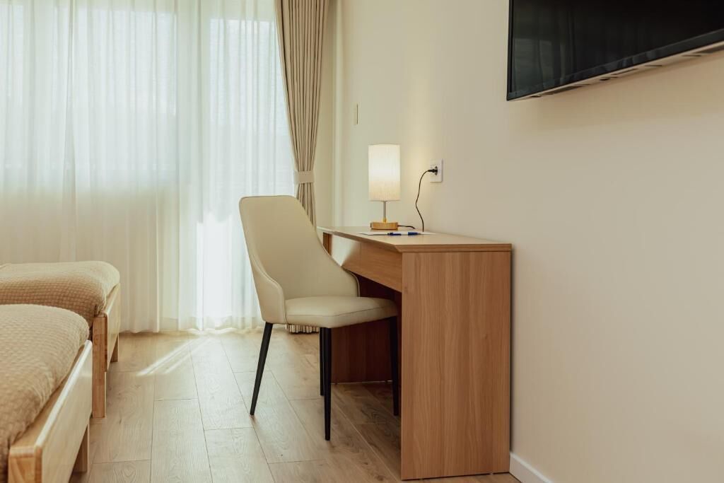 A hotel room with a bed, a desk, a chair, a TV, and a window with curtains.