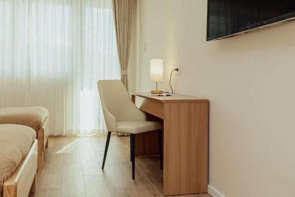 Una habitación de hotel con cama, escritorio, silla, televisión y ventana con cortinas.