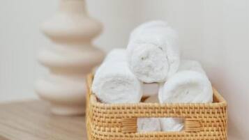 Una cesta de mimbre con toallas blancas enrolladas sobre una superficie de madera.
