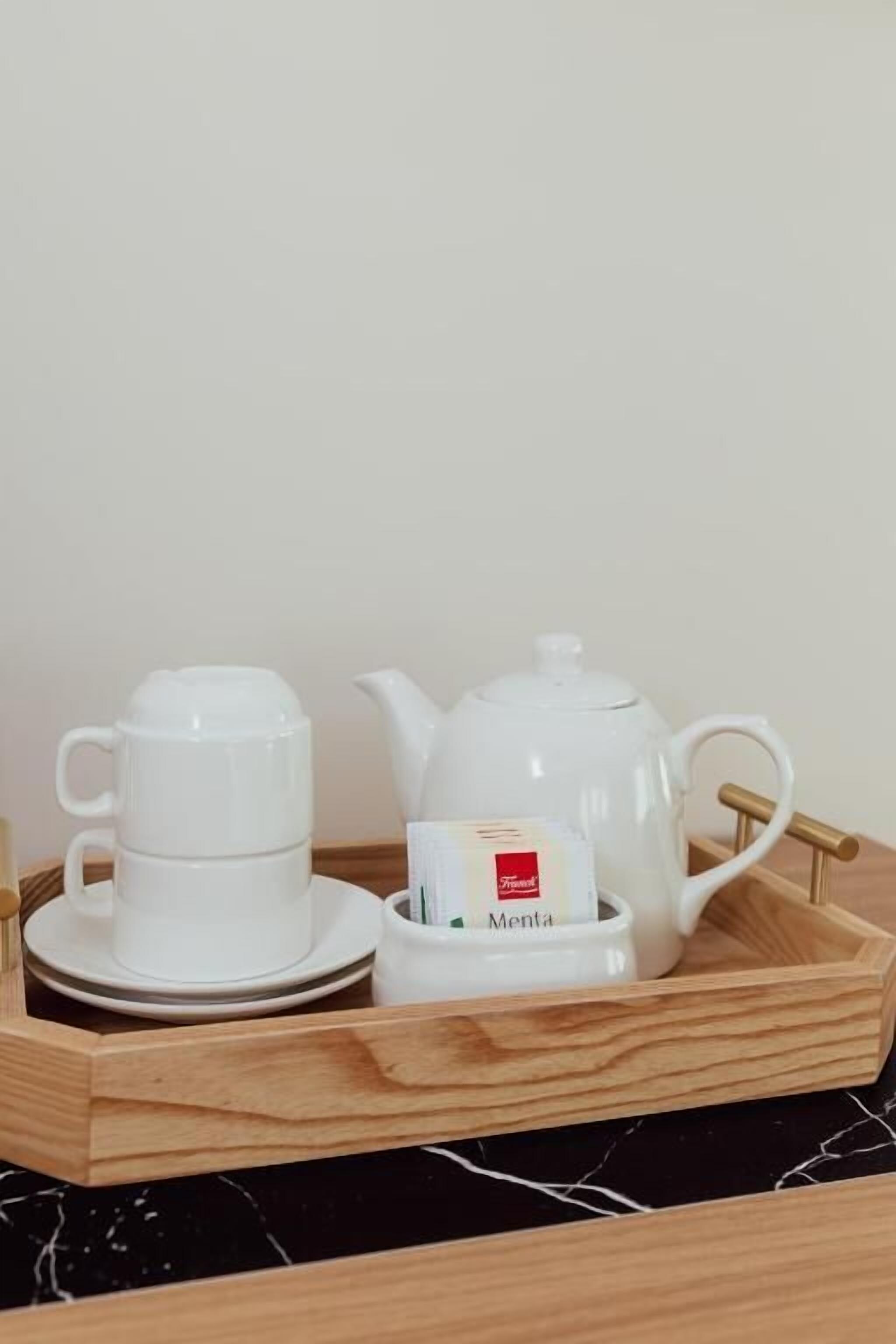 Una bandeja de madera con una tetera blanca, una taza blanca y un platito blanco.