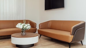 A modern living room with two brown leather sofas, a round wooden coffee table, and a flat-screen TV mounted on the wall. - Hotel Orjen Sport&Pleasure (Trebinje)