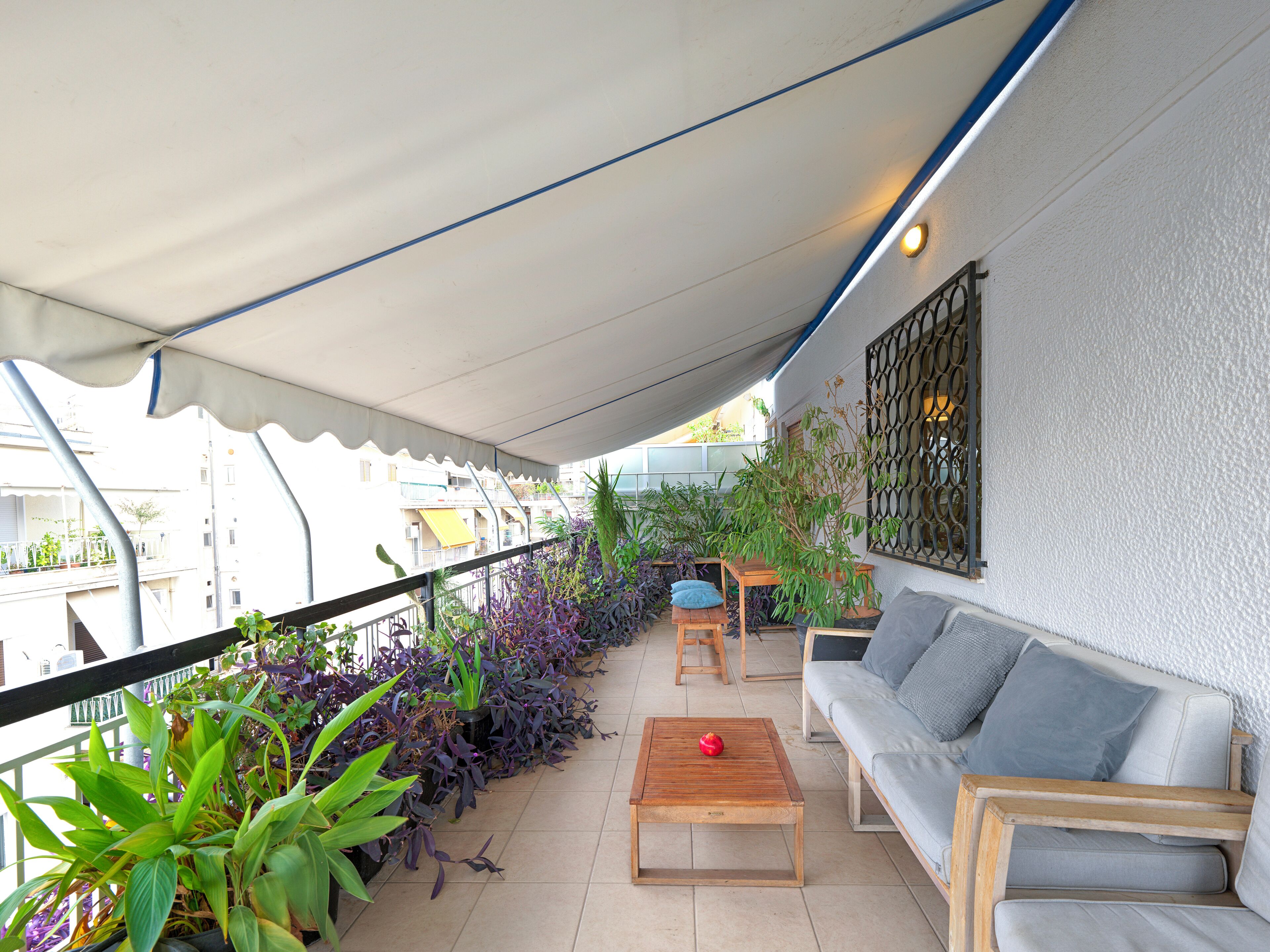 A balcony with a sofa, a wooden table, and potted plants.