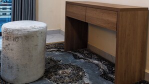 Ein Hotelzimmer mit einem runden Spiegel, einem hölzernen Schminktisch, einem runden Hocker und einem gemusterten Teppich.