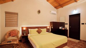 A hotel room with a bed, a chair, a nightstand, a wardrobe, and a door. - Panchavadi Farm Stay (Kumily)
