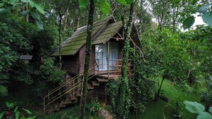 A rustic treehouse with a wooden staircase leading to a balcony with wicker furniture. - Panchavadi Farm Stay (Kumily)