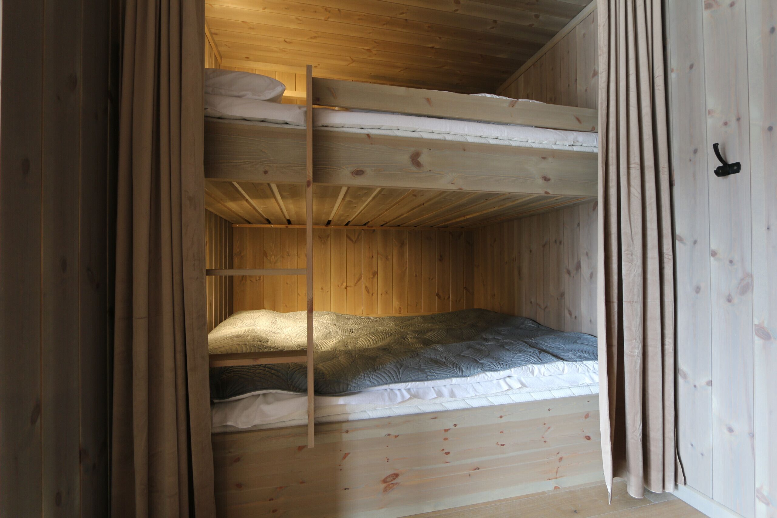 A wooden bunk bed room with a ladder, a single bed, and a door.