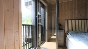 Un dormitorio con cama, una mesita de noche, una puerta corrediza al balcón y vistas a zonas verdes.